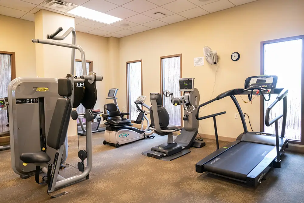 A small Sholom Senior Living gym with various exercise machines, including a treadmill, stationary bike, recumbent bike, and strength training equipment. A small Sholom Senior Living gym with various exercise machines, including a treadmill, stationary bike, recumbent bike, and strength training equipment.